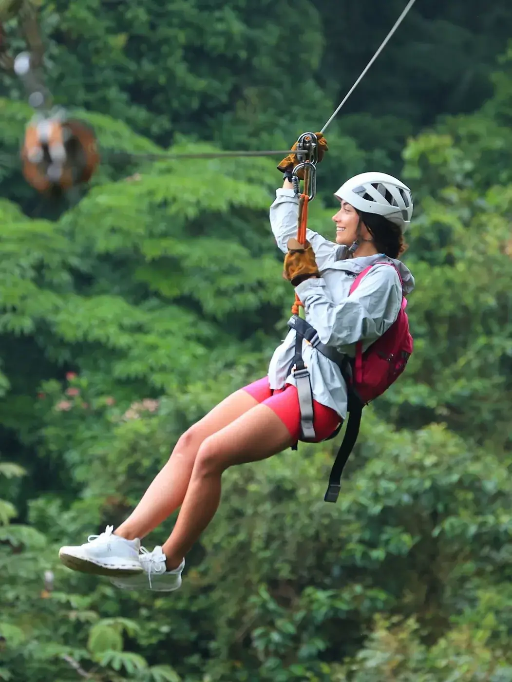 Una visitante con casco se desliza por una tirolesa sobre la selva