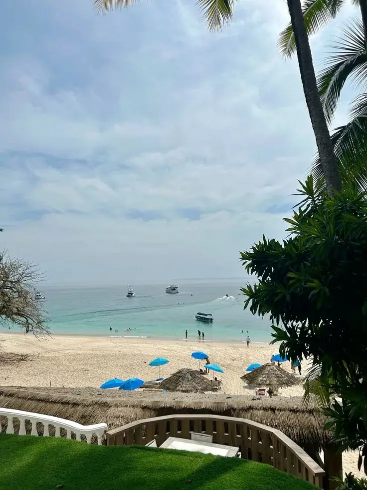 Una playa con sombrillas azules y de palma, vista desde un jardín
