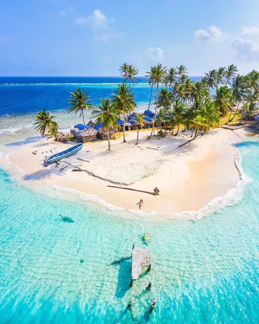 Vista aérea de una isla pequeña con palmeras, cabañas y arena blanca