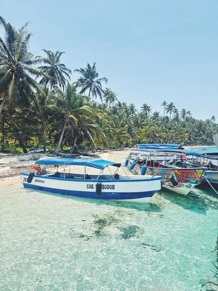 Lanchas de colores en una playa de agua transparente, con palmeras